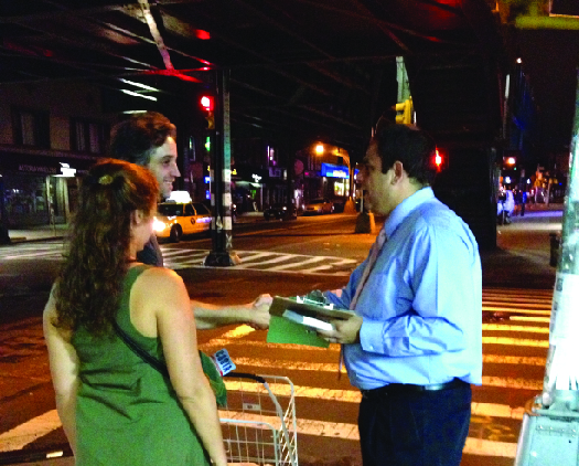 An image of one person holding a clipboard, shaking hands with another person. A third person stands nearby.