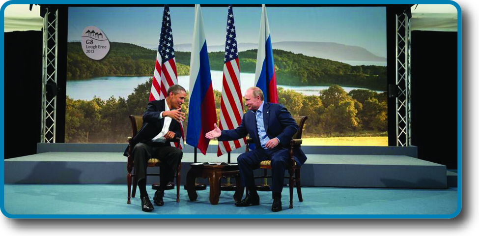 An image of Barack Obama and Vladimir Putin seated in front of two U. S. and two Russian flags, poised to shake hands.