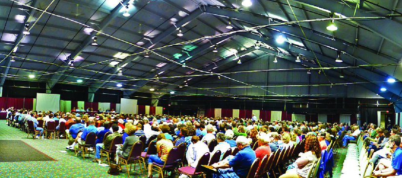 An image of a large group of people sitting in chairs inside of a large room.